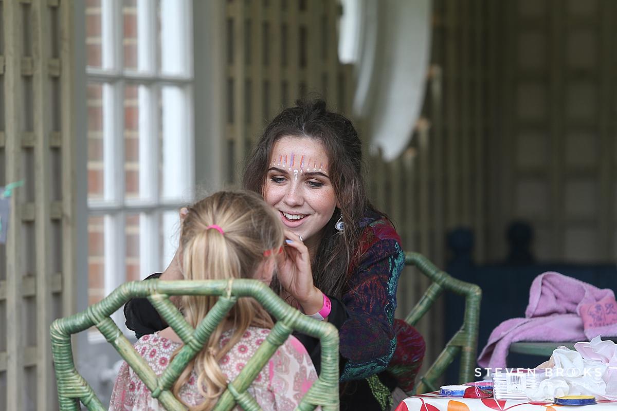 Britain Does Vintage Stody Lodge Norfolk photographer steven brooks photographs a young womans face painting a child at Britain Does Vintage in Norfolk
